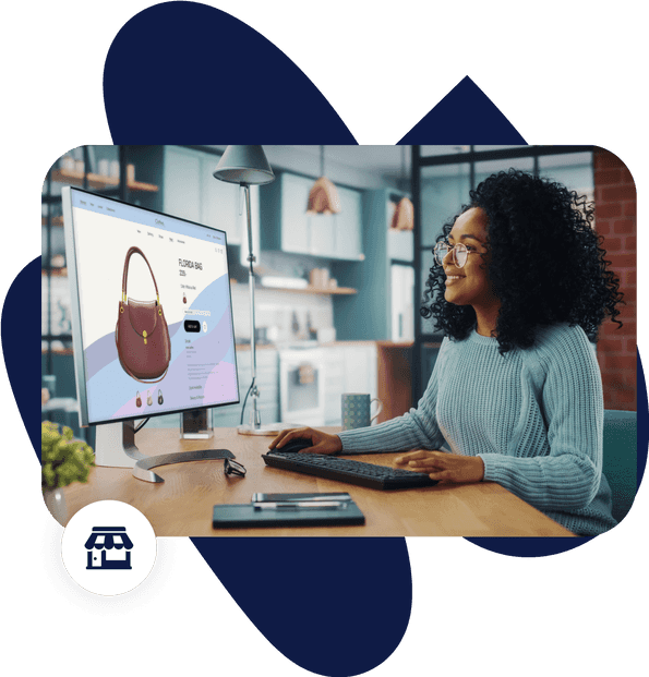 Woman in glasses and thick curly hair smiles at a desk, her computer screen shows a web page selling handbags