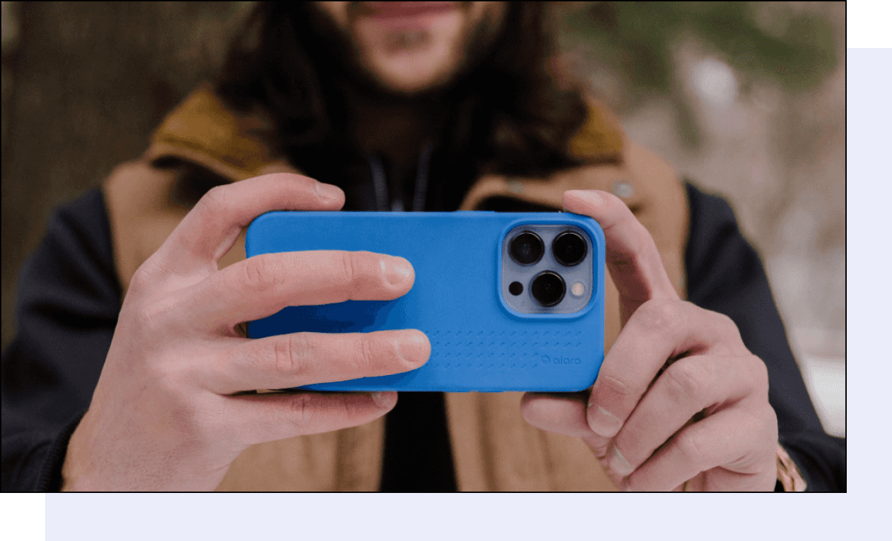 A photo of a person holding a phone with a case on it. The background of the photo is a blurred forest with evergreen trees and fresh snowfall.